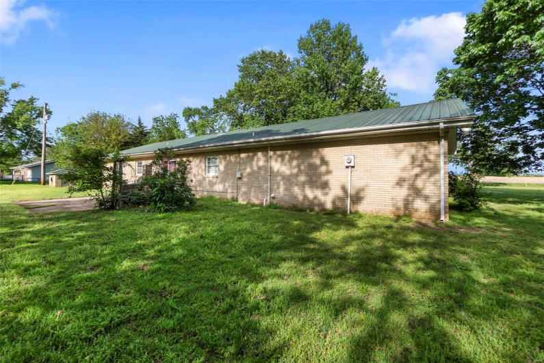 View of side of home featuring a lawn, brick siding, and metal roof
