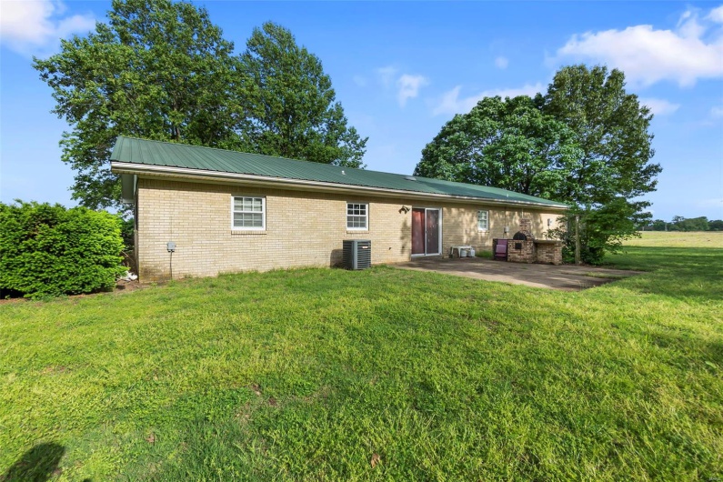 Rear view of house featuring brick siding, central AC unit, a patio area, metal roof, and a yard