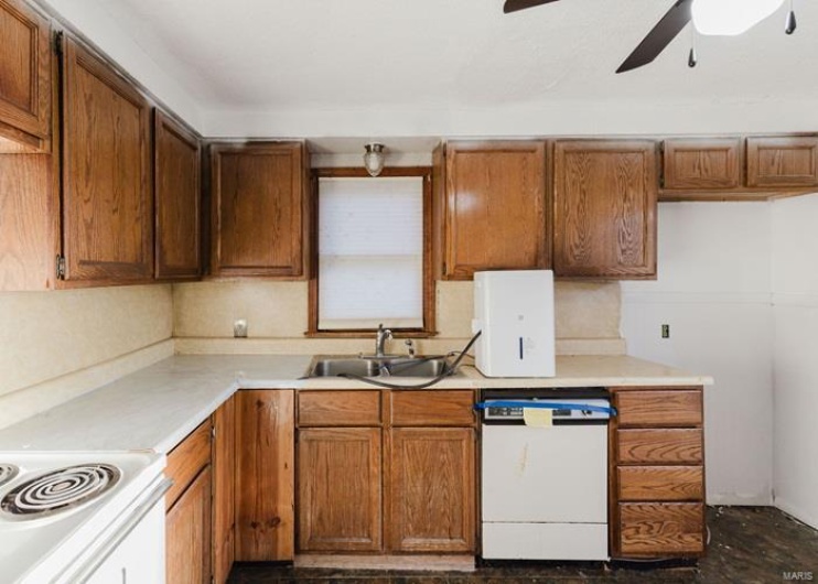 Kitchen with white appliances, ceiling fan, light countertops, brown cabinets, and a sink