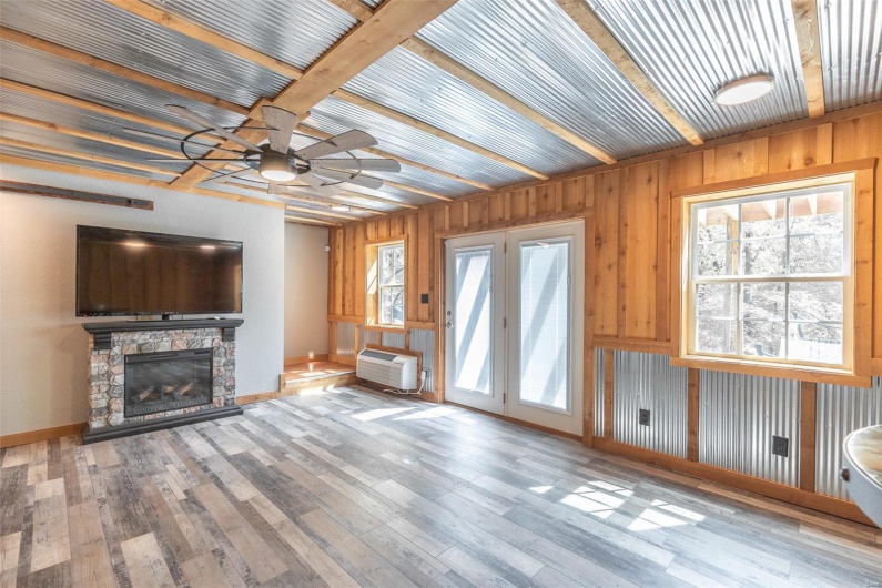 Unfurnished living room with hardwood / wood-style floors, a stone fireplace, baseboards, a wall mounted AC, and a ceiling fan