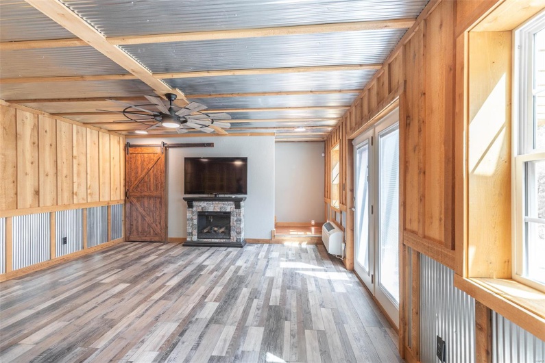 Unfurnished living room featuring wood finished floors, baseboards, a stone fireplace, ceiling fan, and a barn door