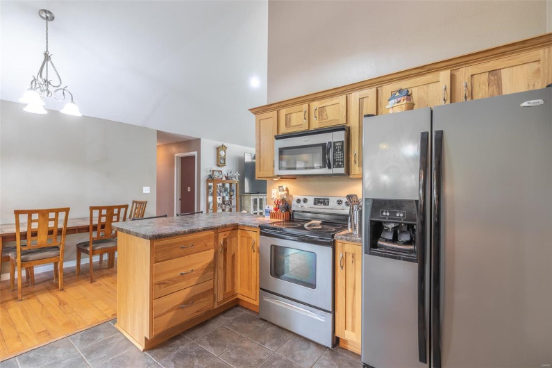 Kitchen with dark countertops, appliances with stainless steel finishes, a peninsula, decorative light fixtures, and a towering ceiling