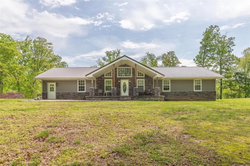 Ranch-style house featuring stone siding, metal roof, and a front yard