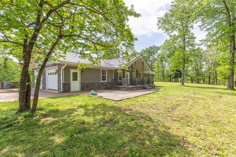Rear view of property with stone siding, a yard, metal roof, an attached garage, and driveway