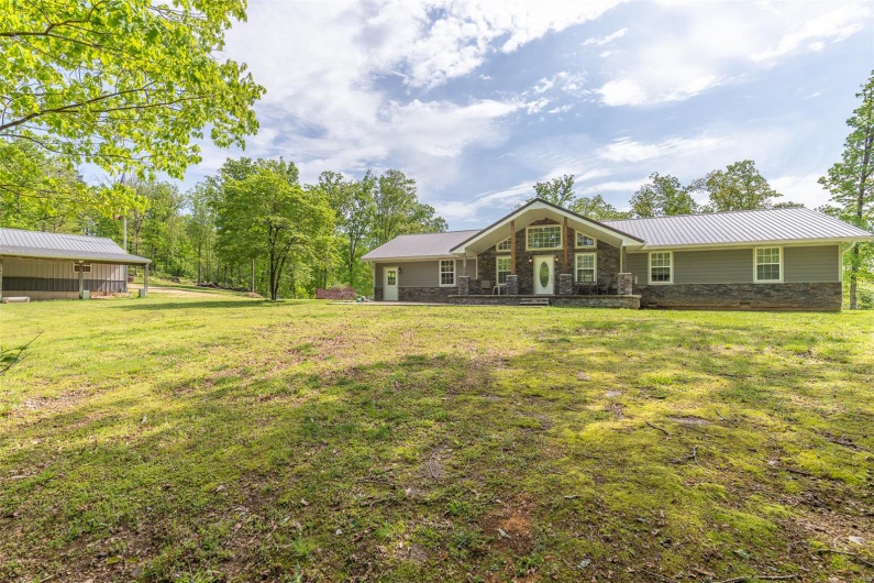 Back of house featuring a lawn, metal roof, and stone siding