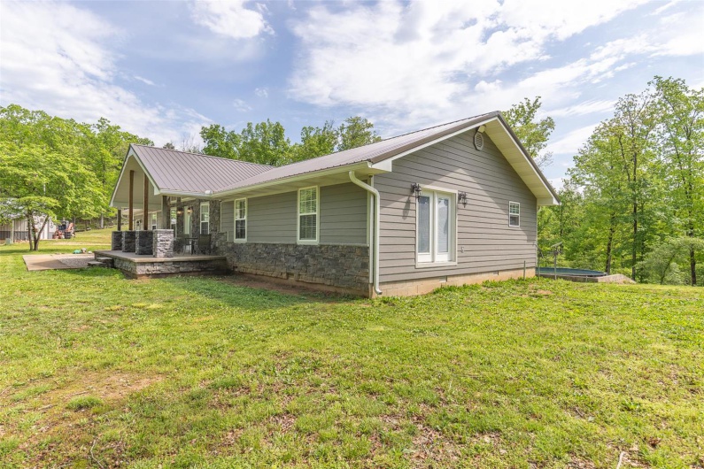 View of side of property with a yard, metal roof, and stone siding