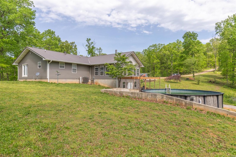 Back of property featuring a yard, central AC, metal roof, and an outdoor pool