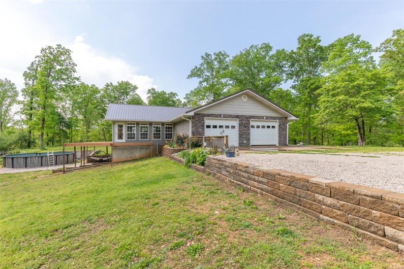 Ranch-style house featuring a garage, stone siding, a front yard, metal roof, and driveway