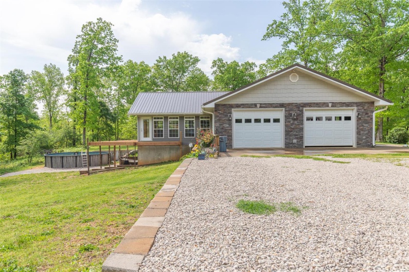 View of front of property featuring a front yard, stone siding, gravel driveway, a jacuzzi, and metal roof