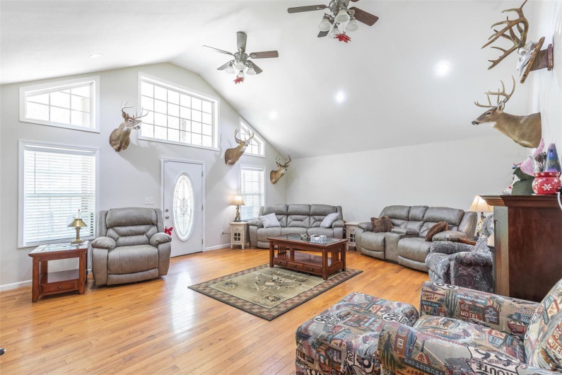 Living area with high vaulted ceiling, baseboards, a ceiling fan, and hardwood / wood-style floors