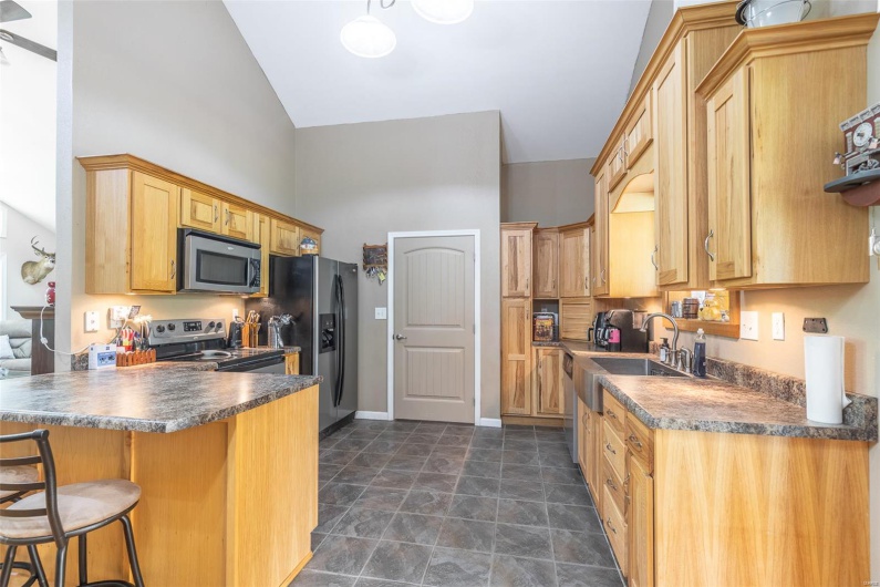 Kitchen featuring dark countertops, appliances with stainless steel finishes, a sink, high vaulted ceiling, and a peninsula
