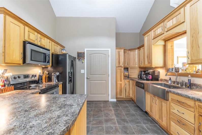 Kitchen with light brown cabinets, dark countertops, high vaulted ceiling, a sink, and stainless steel appliances