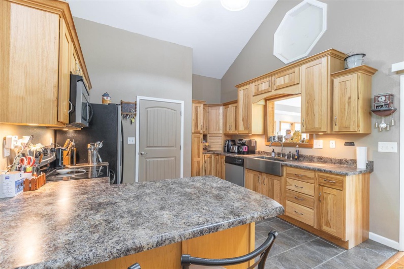 Kitchen featuring a peninsula, lofted ceiling, dark tile patterned flooring, a sink, and stainless steel appliances