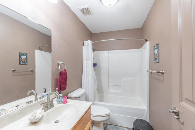 Bathroom featuring toilet, visible vents, shower / bathtub combination with curtain, and vanity
