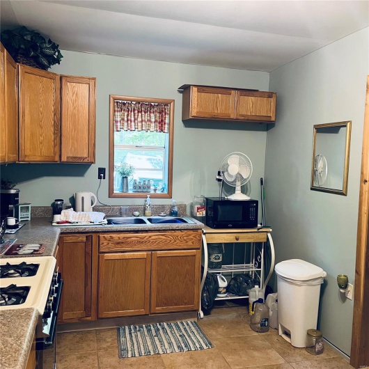 Kitchen with brown cabinetry, a sink, range with gas stovetop, and black microwave