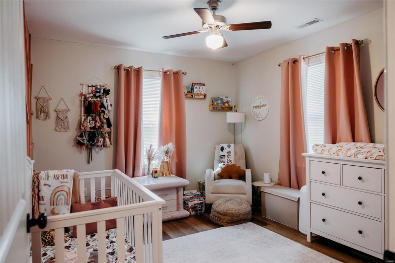 Bedroom featuring a nursery area, ceiling fan, visible vents, wood finished floors