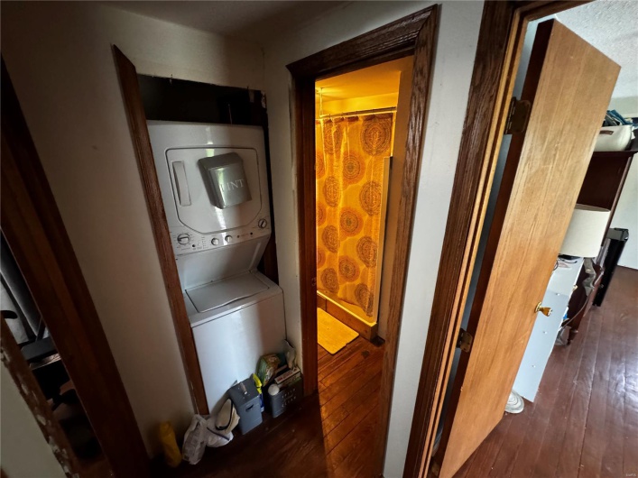 Laundry area featuring wood-type flooring and stacked washer / dryer
