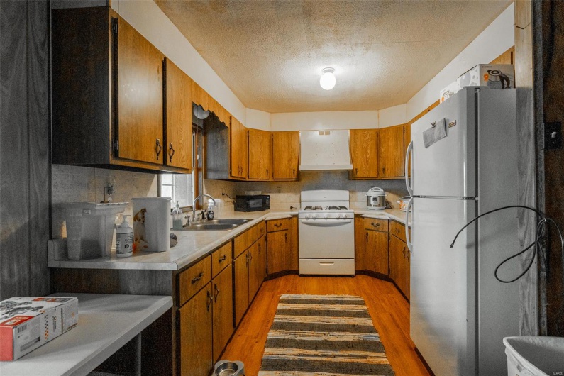 Kitchen with a sink, brown cabinetry, white appliances, light wood-type flooring, and light countertops