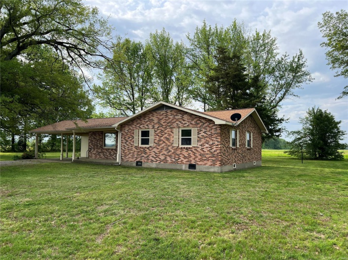 View of property exterior featuring a yard, brick siding, and a carport