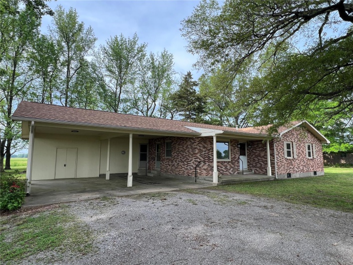 Ranch-style home featuring gravel driveway, brick siding, and a carport
