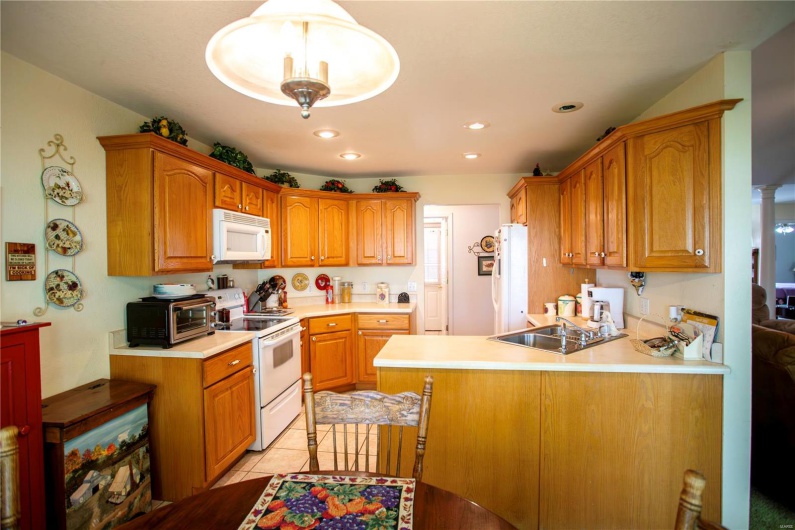 Kitchen featuring a peninsula, white appliances, brown cabinets, a toaster, and light countertops