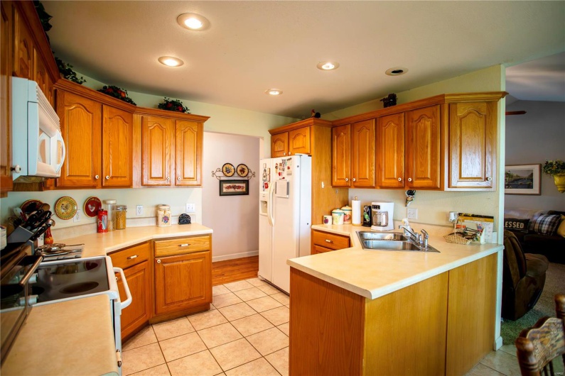 Kitchen with brown cabinets, a sink, white appliances, light countertops, and recessed lighting