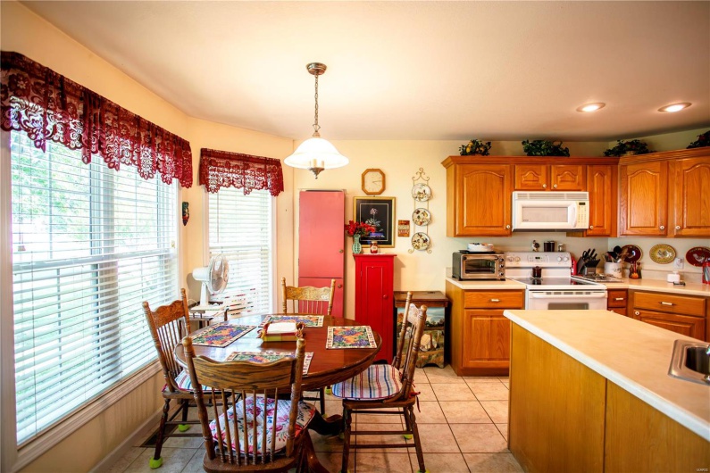 Kitchen with brown cabinets, white appliances, a healthy amount of sunlight, and light countertops