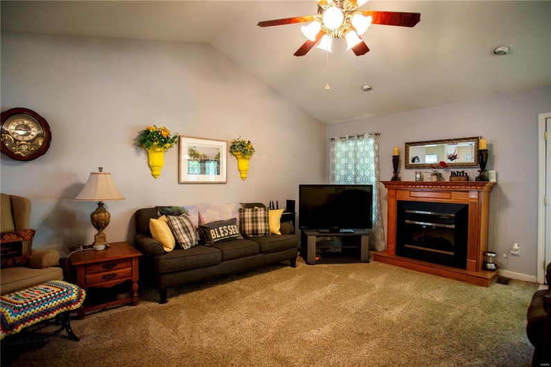 Carpeted living room featuring vaulted ceiling, a ceiling fan, and a glass covered fireplace