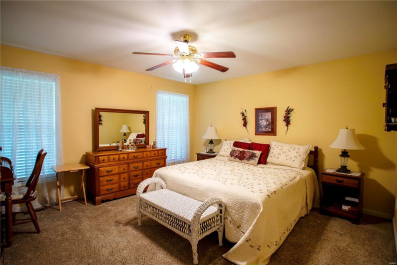 Carpeted bedroom with a ceiling fan and multiple windows