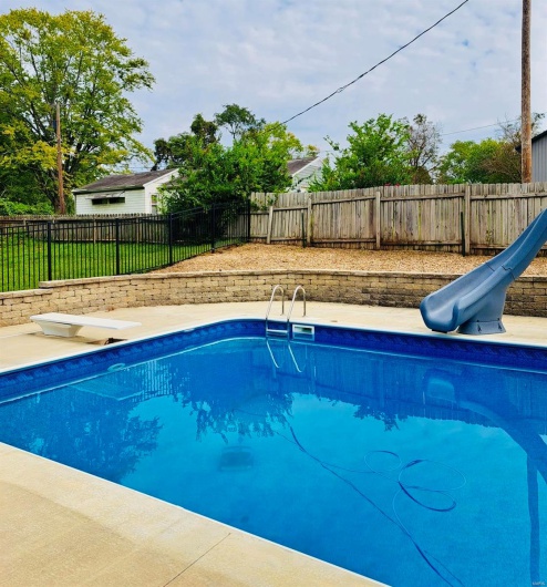 View of swimming pool with a water slide, a fenced backyard, and a diving board