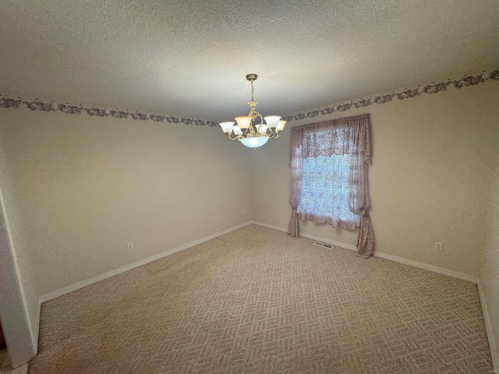 Empty room with carpet floors, an inviting chandelier, and a textured ceiling