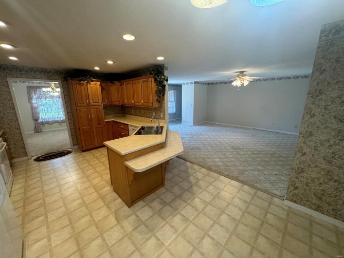 Kitchen featuring a breakfast bar, sink, ceiling fan with notable chandelier, kitchen peninsula, and light colored carpet