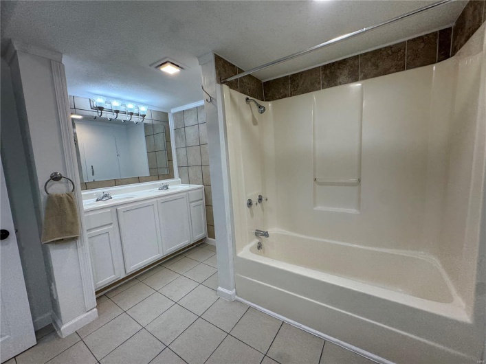 Full bath featuring double vanity, tile patterned floors, a sink, and shower / washtub combination