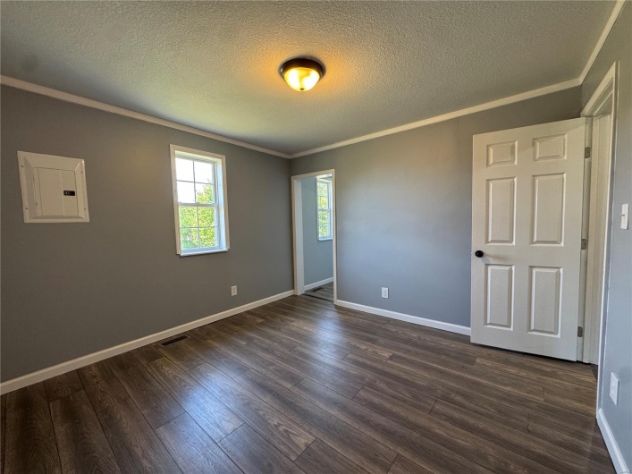 Spare room with a textured ceiling, baseboards, ornamental molding, dark wood finished floors, and electric panel