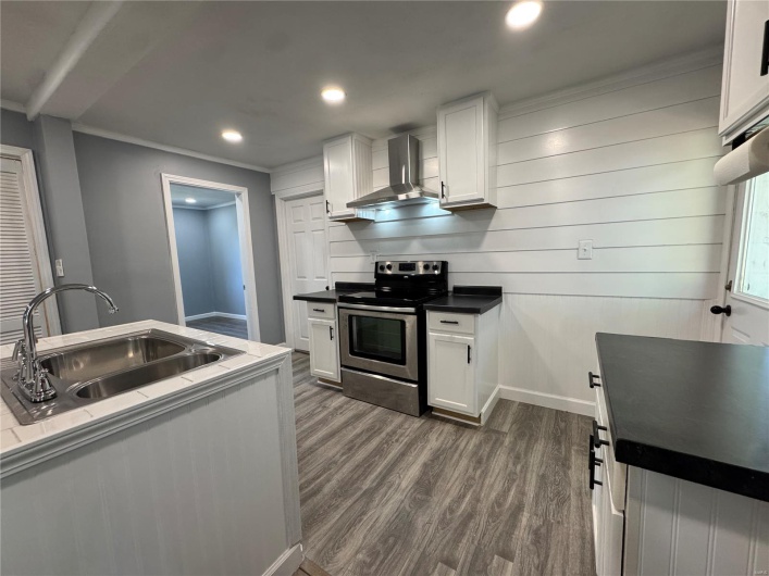 Kitchen featuring a sink, white cabinets, dark wood finished floors, wall chimney exhaust hood, and electric range