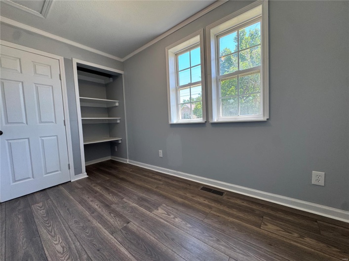 Unfurnished bedroom featuring a closet, visible vents, crown molding, dark wood-style floors, and baseboards