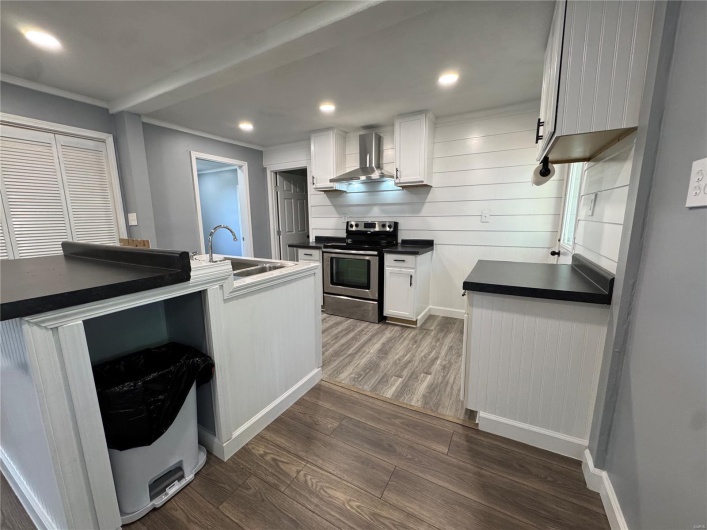 Kitchen with dark wood-style flooring, wall chimney range hood, stainless steel electric range, and a sink