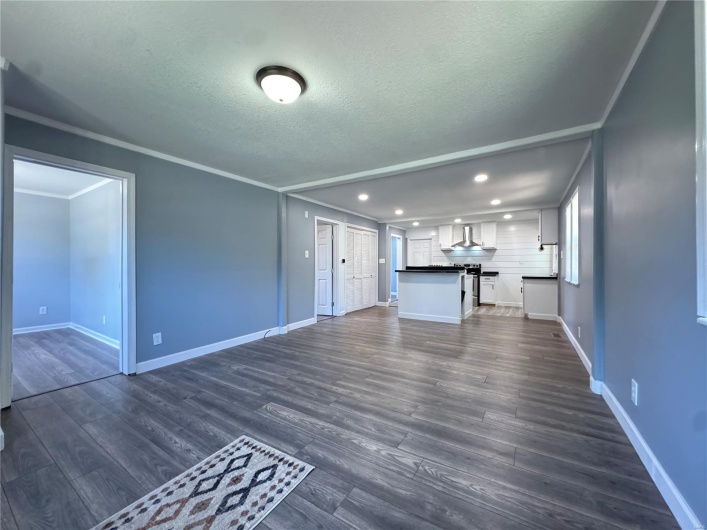 Unfurnished living room with a textured ceiling, baseboards, dark wood-type flooring, and recessed lighting