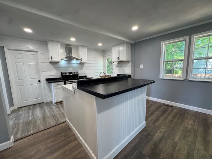 Kitchen featuring baseboards, stainless steel range with electric cooktop, dark wood-type flooring, wall chimney range hood, and dark countertops
