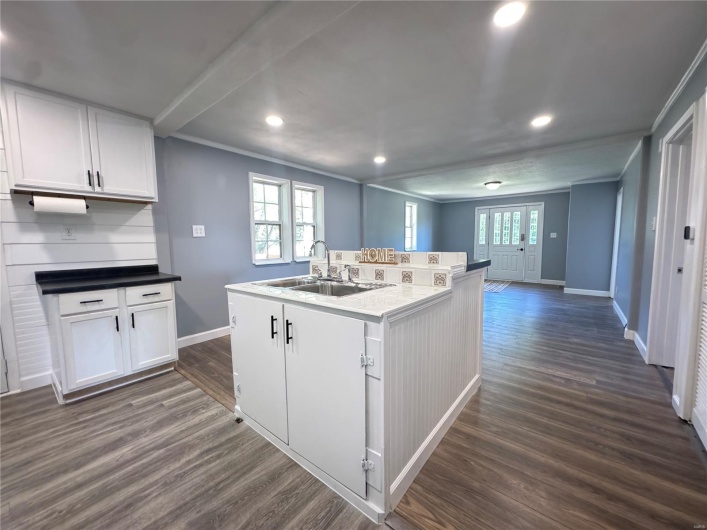 Kitchen featuring white cabinetry, baseboards, dark wood-style floors, and a sink