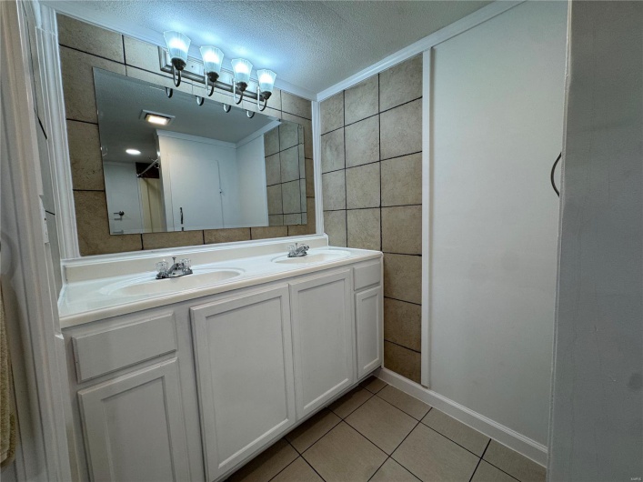 Full bathroom with a sink, tile walls, tile patterned flooring, crown molding, and double vanity