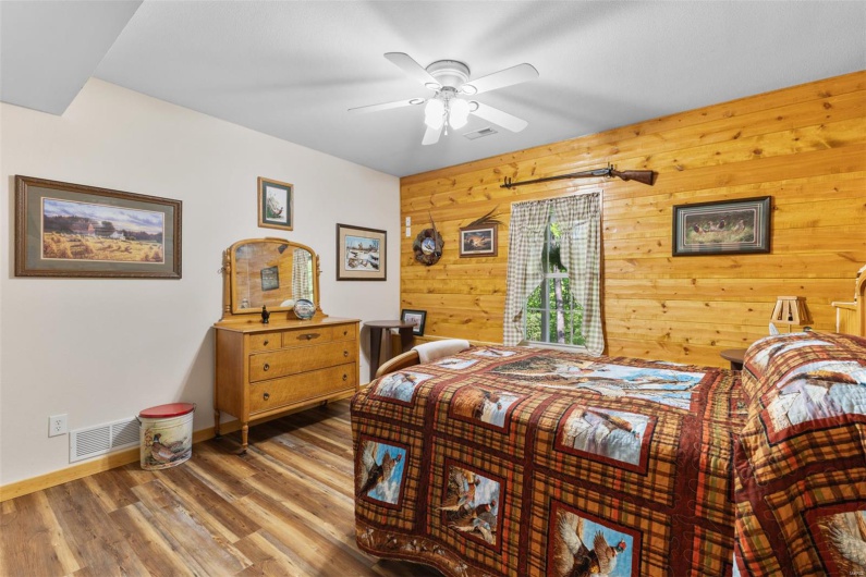 Bedroom with a ceiling fan, baseboards, visible vents, wood walls, and wood finished floors