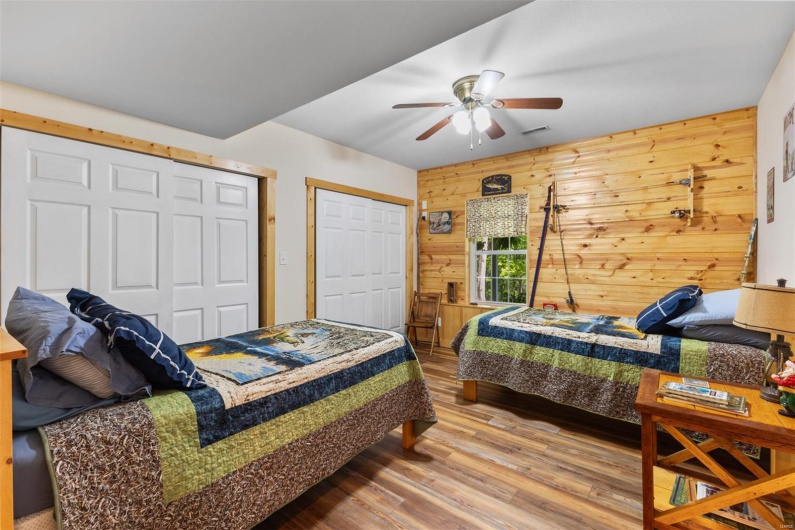 Bedroom with ceiling fan, wooden walls, visible vents, and wood finished floors