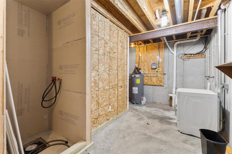 Unfinished below grade area featuring water heater and washer / clothes dryer