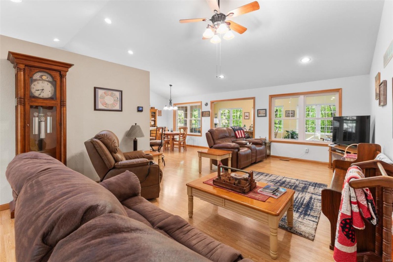 Living room with lofted ceiling, recessed lighting, light wood-type flooring, and ceiling fan with notable chandelier