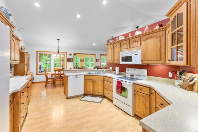 Kitchen with a sink, a peninsula, white appliances, light wood-style flooring, and glass insert cabinets