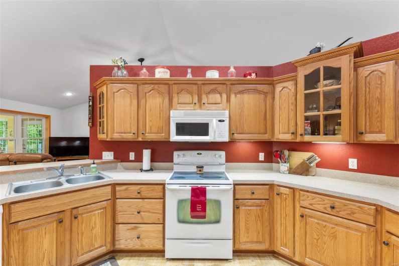 Kitchen featuring a sink, lofted ceiling, white appliances, light countertops, and glass insert cabinets