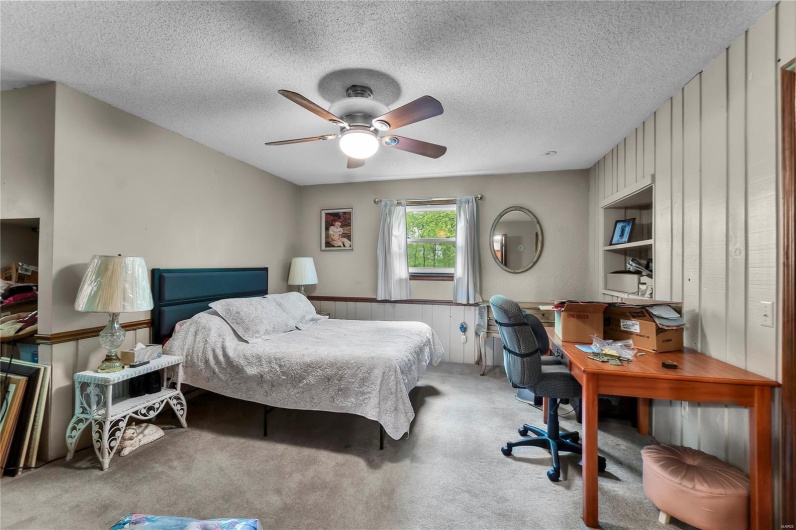 Carpeted bedroom with a textured ceiling, wooden walls, and ceiling fan