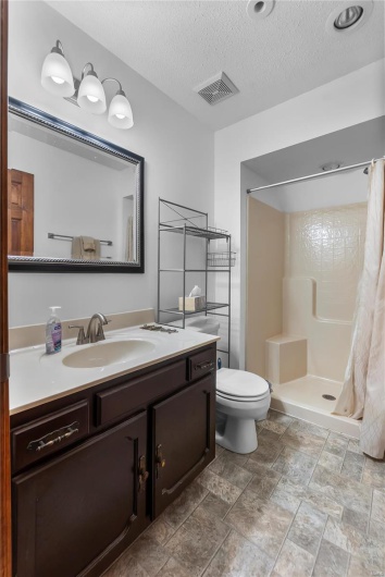 Full bath featuring a textured ceiling, toilet, visible vents, a shower stall, and vanity
