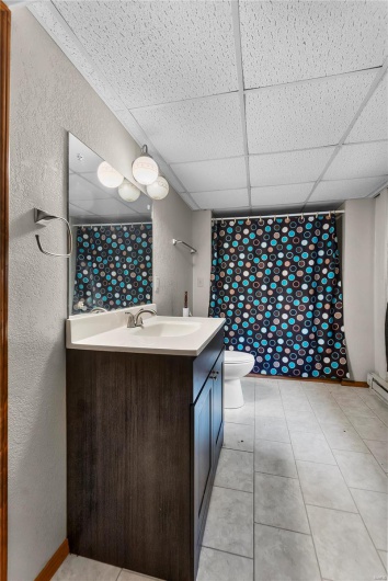 Basement Bathroom with toilet, a shower with shower curtain, vanity, and a paneled ceiling